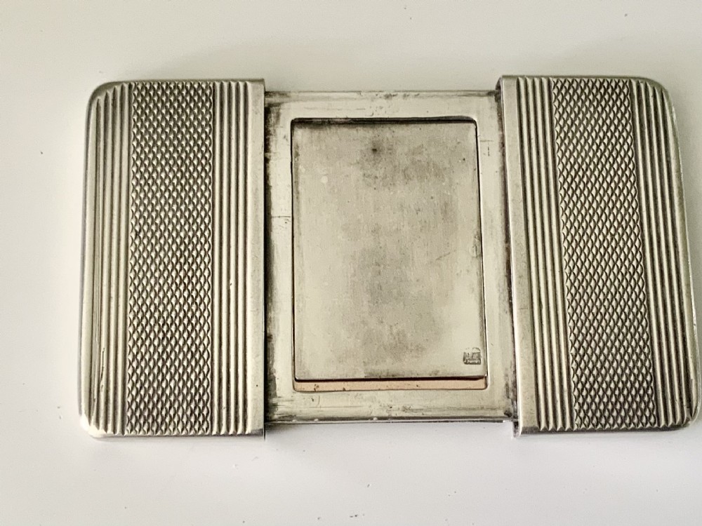 An Art Deco silver travelling photograph frame with engine-turned geometric patterns on the sliding outer panels, displaying a black and white portrait. View V