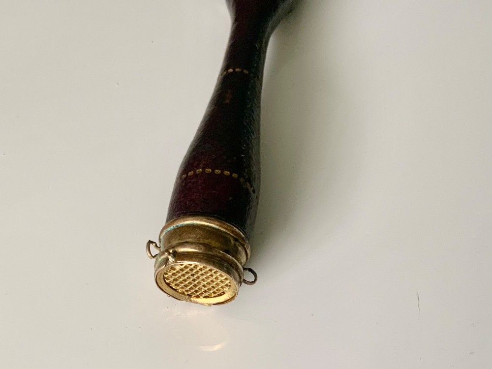A 19th-century French hand fan featuring a dark brown leather handle with an integrated gilt metal vinaigrette grille at the base and a pleated purple leaf. View II