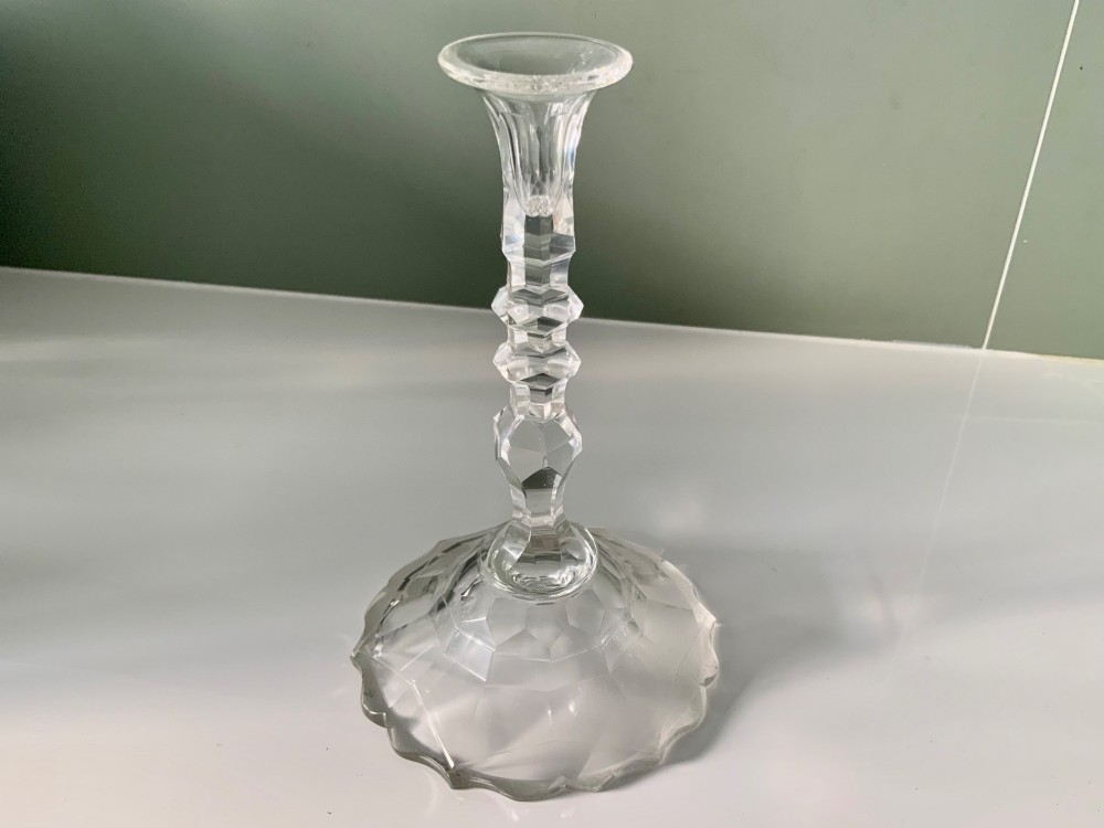 A Georgian clear glass taper stick featuring a faceted knopped stem and a scalloped, facet-cut domed base.