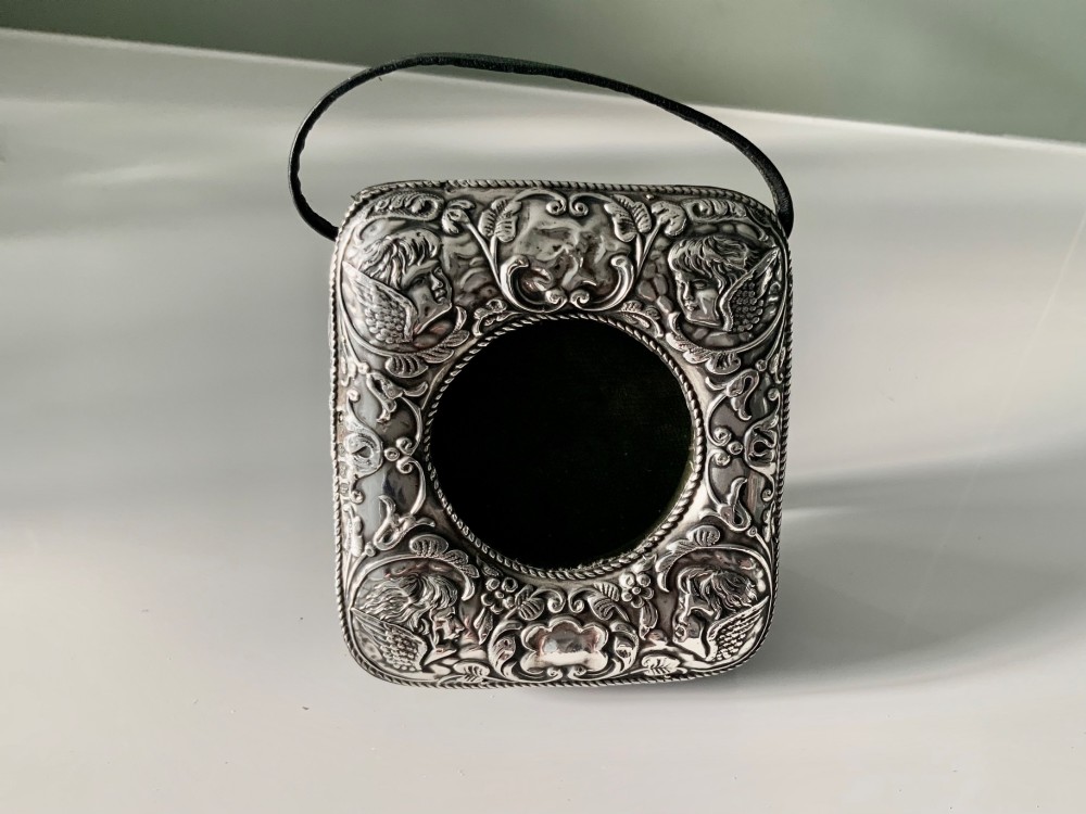 An embossed silver pocket watch stand featuring the Reynolds Angels cherub motif with a circular opening and velvet lining.