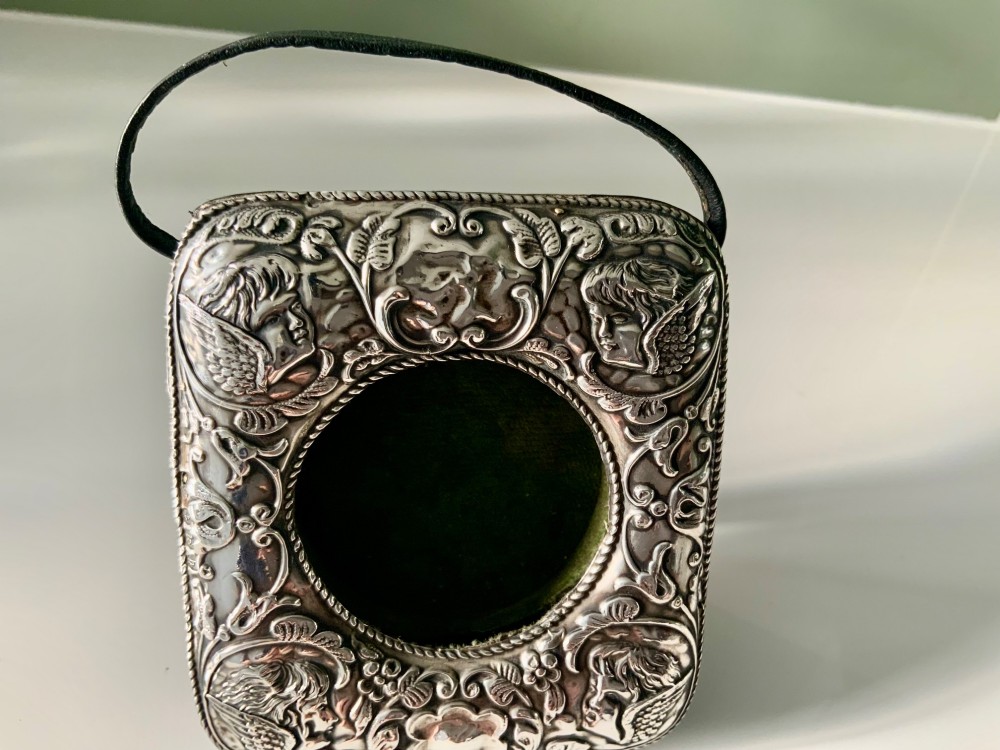 An embossed silver pocket watch stand featuring the Reynolds Angels cherub motif with a circular opening and velvet lining. View IV