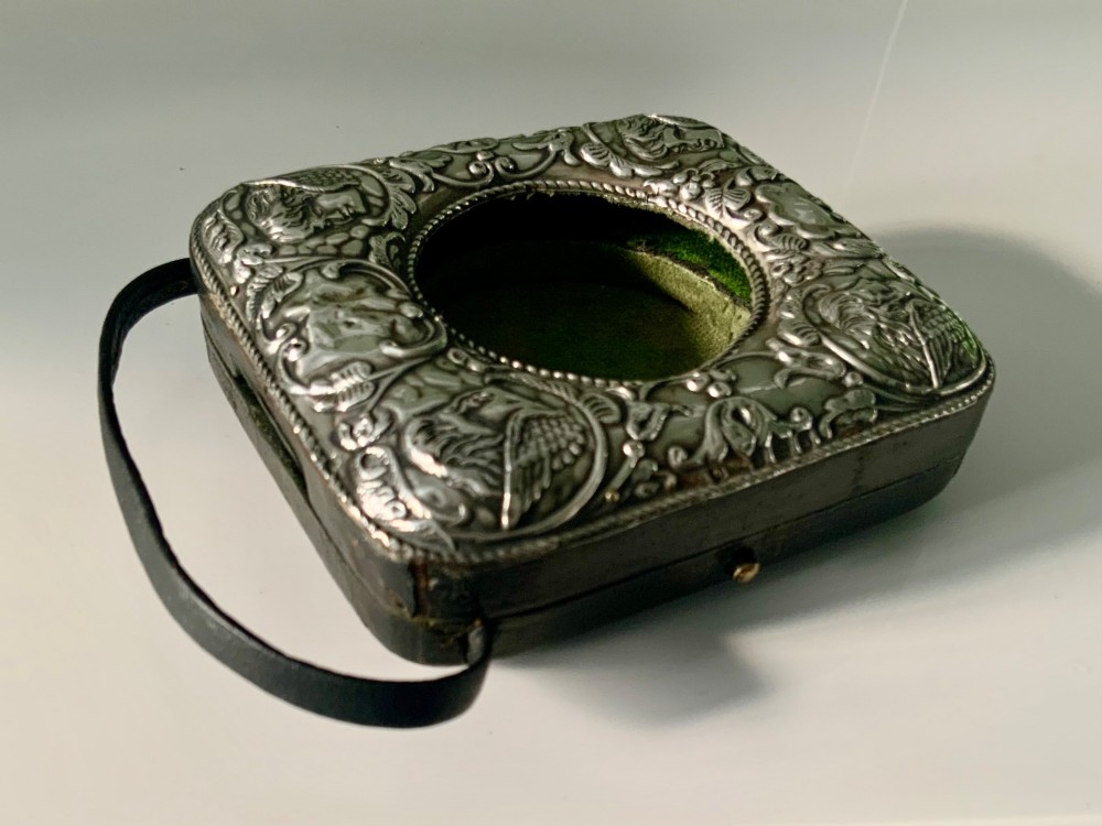 An embossed silver pocket watch stand featuring the Reynolds Angels cherub motif with a circular opening and velvet lining. View IX