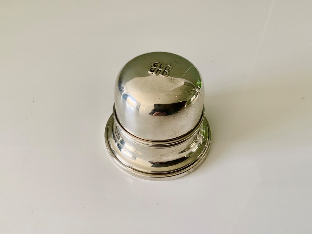 A domed sterling silver ring box resting on a stepped circular base with an embossed logo on top.
