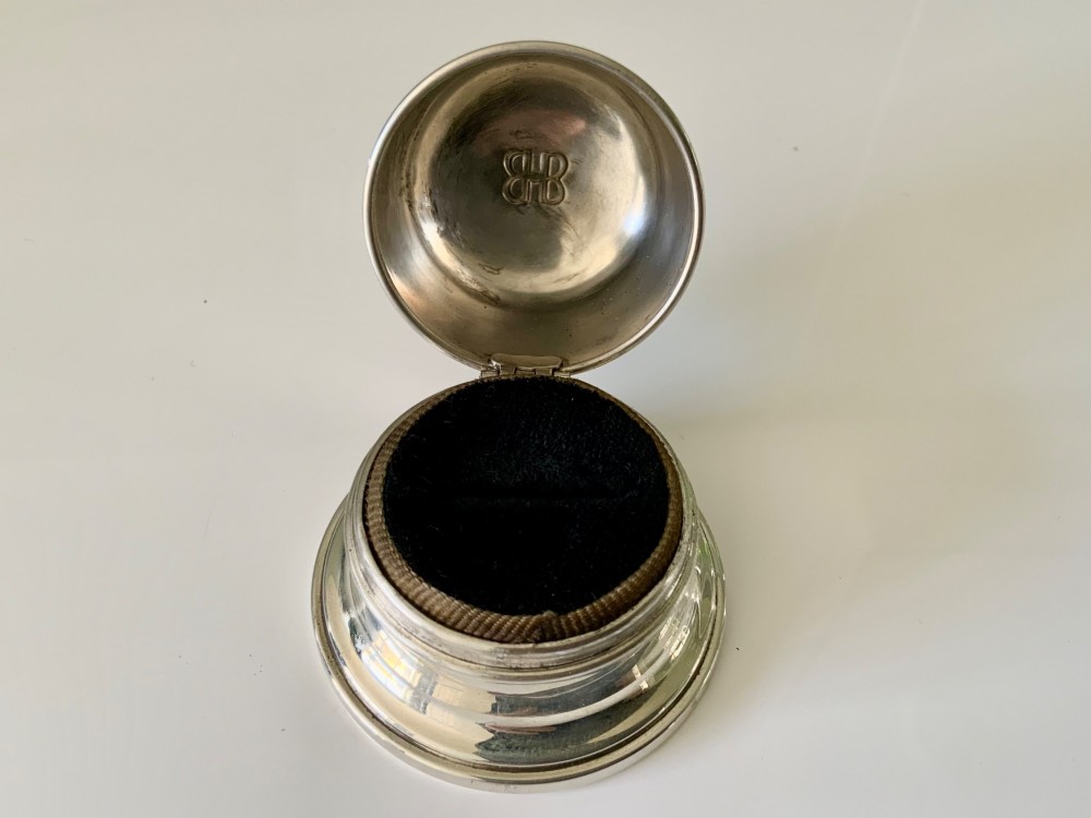 A domed sterling silver ring box resting on a stepped circular base with an embossed logo on top. View III