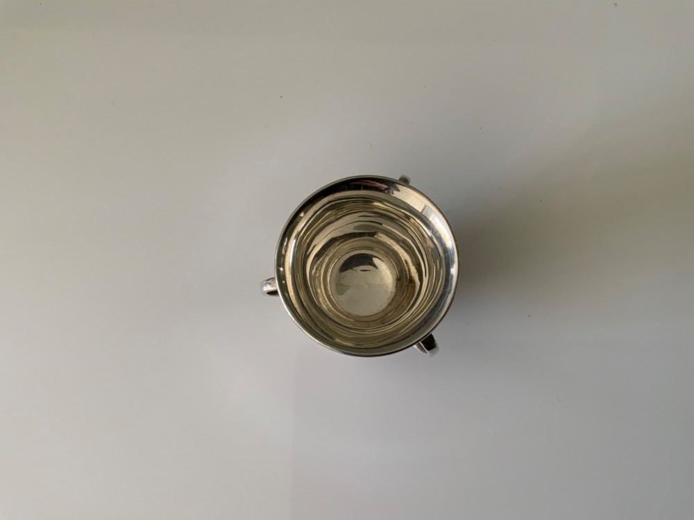 A polished miniature silver tyg featuring a flared rim, three looped handles, and a stepped pedestal base. View III