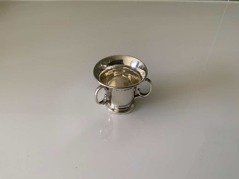 A polished miniature silver tyg featuring a flared rim, three looped handles, and a stepped pedestal base. View IV