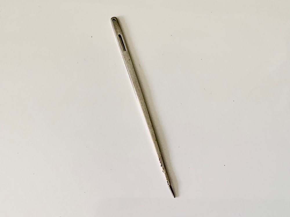 An elongated early 18th-century silver bodkin featuring engraved initials, a slotted eye, and a terminal hole. View II