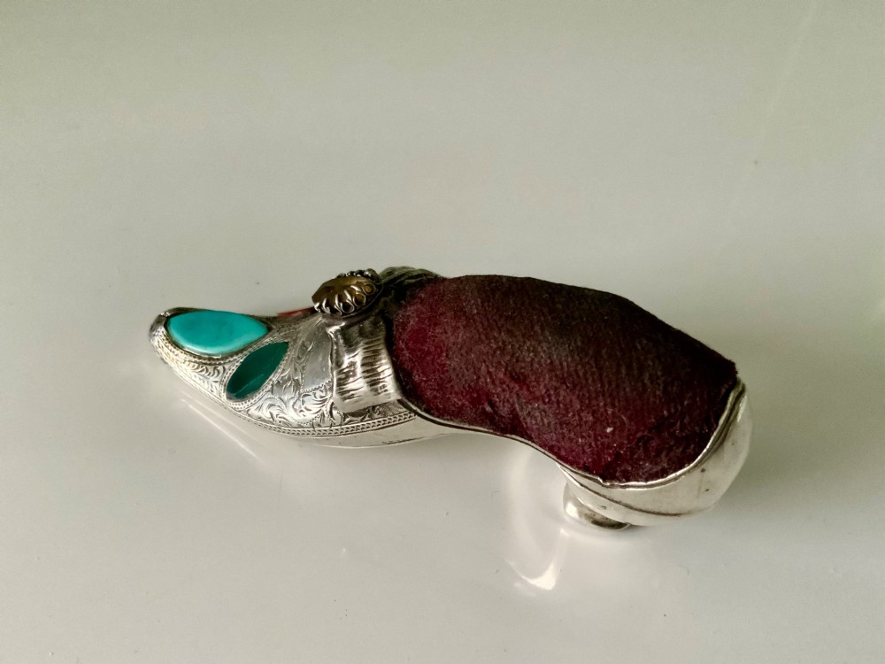 A Victorian silver shoe-shaped pin cushion embellished with hand engraving, set agate stones, and a dark velvet cushion top. View II