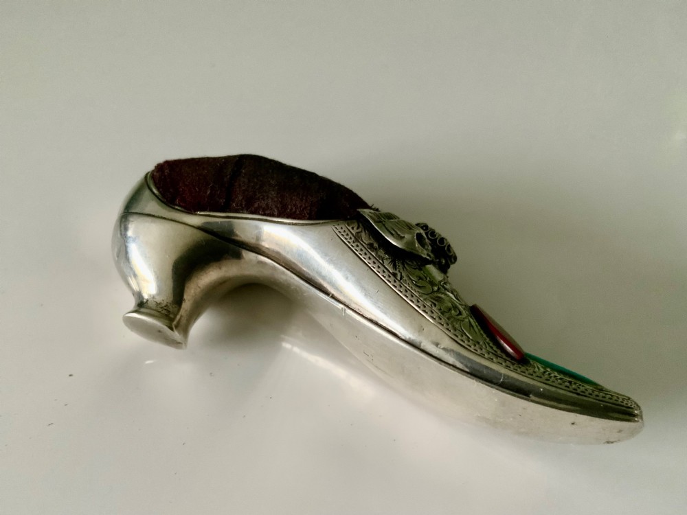 A Victorian silver shoe-shaped pin cushion embellished with hand engraving, set agate stones, and a dark velvet cushion top. View VII