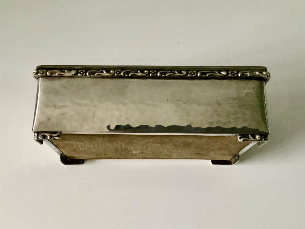 A rectangular silver plated box featuring a hand-hammered lid and a dark oval central inset framed by decorative detailing. View V
