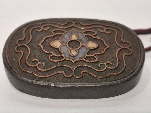 fig 1. An oval-shaped pewter Japanese manju netsuke featuring champleve enamel floral decoration and an attached cord.