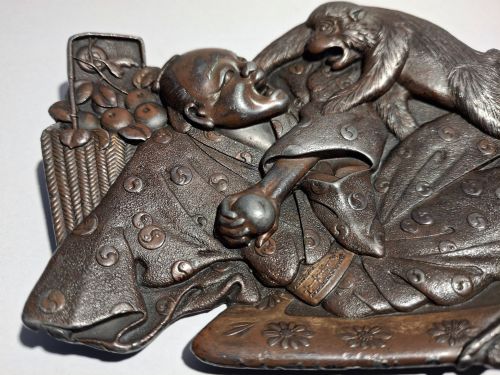 fig 3. A dark bronze Japanese Takazogan metal tray depicting a figure in patterned robes reacting to a monkey perched on his shoulder.