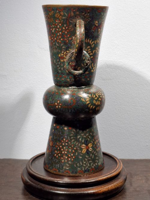 fig 1. A miniature Japanese cloisonne enamel ritual vase with two loop handles, loose rings, and polychrome floral decoration on a dark green background.