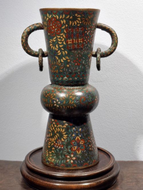 fig 2. A miniature Japanese cloisonne enamel ritual vase with two loop handles, loose rings, and polychrome floral decoration on a dark green background.