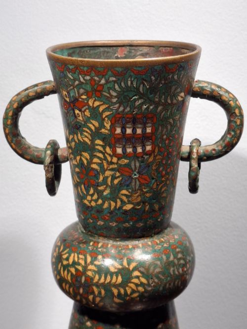 fig 3. A miniature Japanese cloisonne enamel ritual vase with two loop handles, loose rings, and polychrome floral decoration on a dark green background.