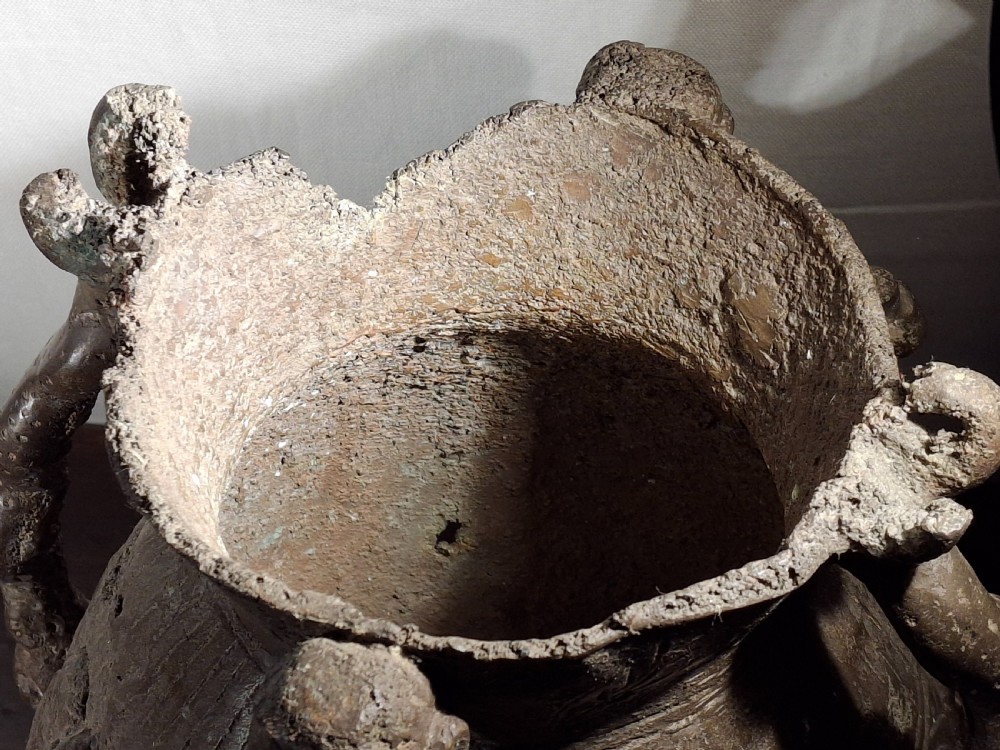 A cast bronze vessel with raised relief figures, twin looped handles, and geometric surface markings. View IX