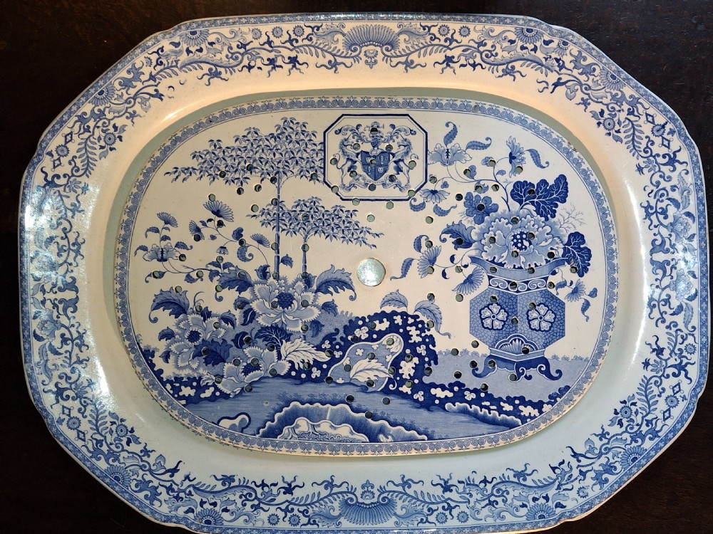 An oval blue and white underglaze transferware ceramic meat platter with a perforated drainer insert decorated with chinoiserie motifs and a coat of arms.