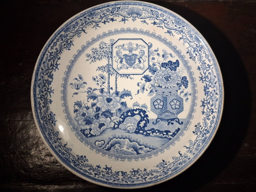 A circular blue and white transferware compote dish featuring a central armorial coat of arms and chinoiserie floral motifs.