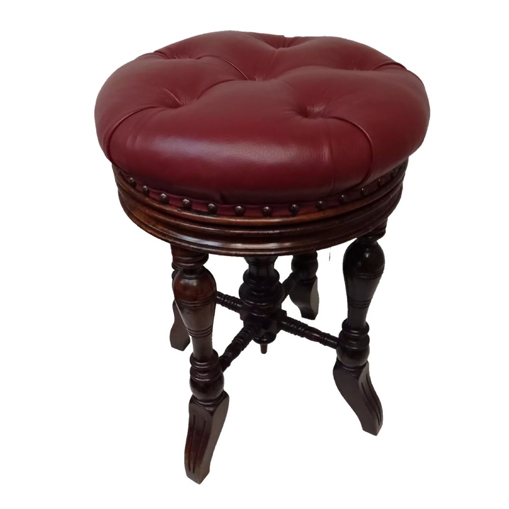 A late Victorian walnut revolving piano stool featuring a circular button-tufted red leather seat, brass studded trim, and four turned legs with a central height adjustment thread.