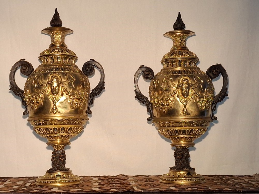 A pair of 19th-century French gilt bronze cassolettes featuring mask reliefs, pierced necks, twin scroll handles, and flame finials.