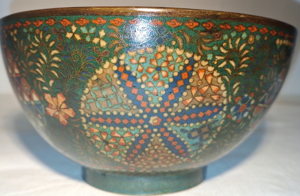 A circular Japanese cloisonne bowl decorated with green ground, geometric star patterns, and floral enamel scrollwork.