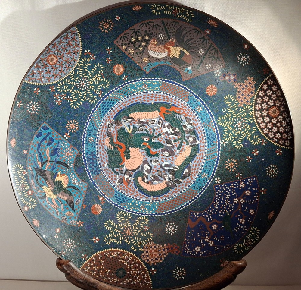 A large circular dark blue Japanese cloisonne enamel charger decorated with a central dragon motif and surrounding fan-shaped panels.