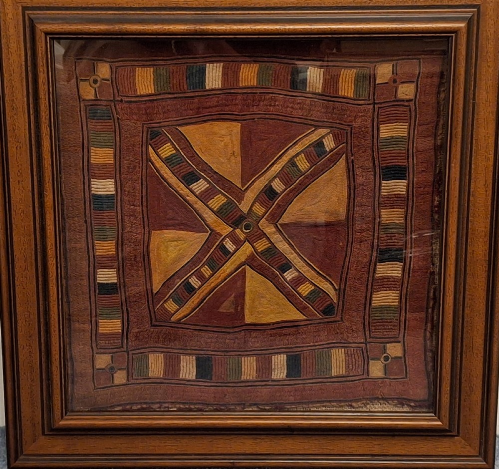 A framed square antique Indian Banjara textile panel featuring geometric embroidery in rust, ochre, green, and dark navy threads.