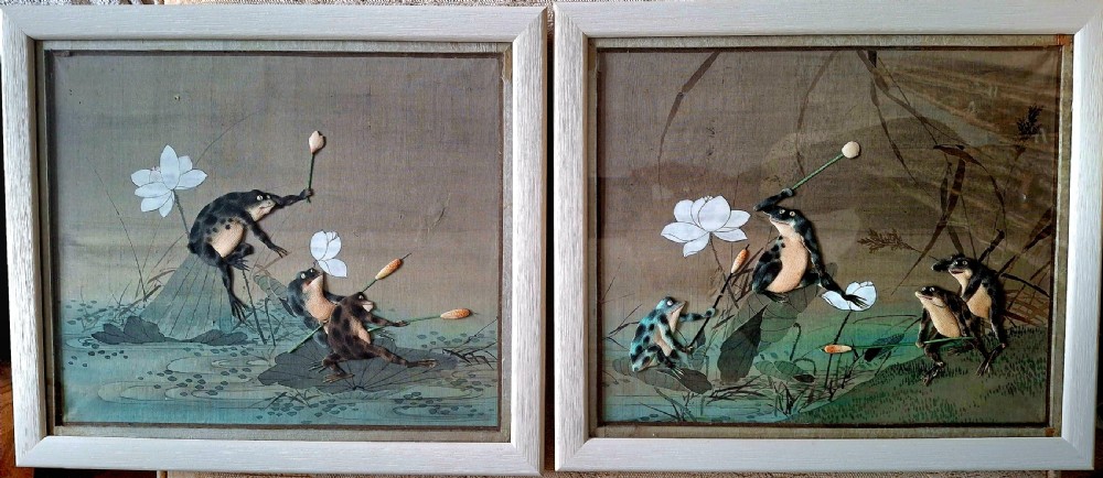 A framed pair of Japanese late nineteenth-century silk paintings depicting anthropomorphic frogs fighting with lotus flowers and reeds.