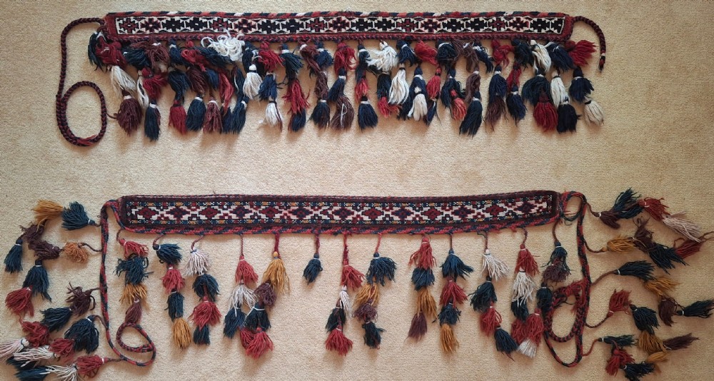 A pair of handwoven wool Turkoman camel neck trappings featuring geometric red and cream bands trimmed with dense multicoloured tassels.