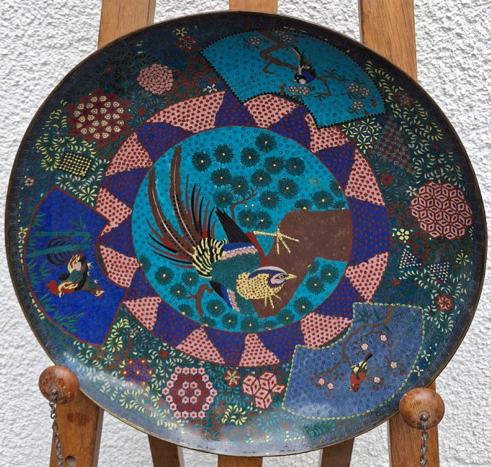 A large circular Japanese cloisonne enamel charger depicting a central bird on a branch surrounded by floral and geometric pattern fields.