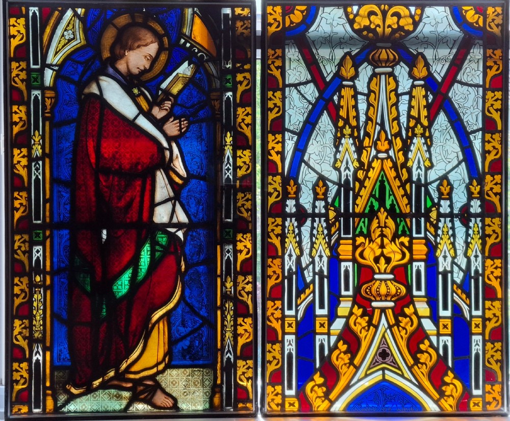 A pair of rectangular nineteenth-century Gothic Revival stained glass panels featuring a saintly figure holding a book on one panel and intricate architectural tracery on the second in cobalt blue, ruby red, and gold tones.