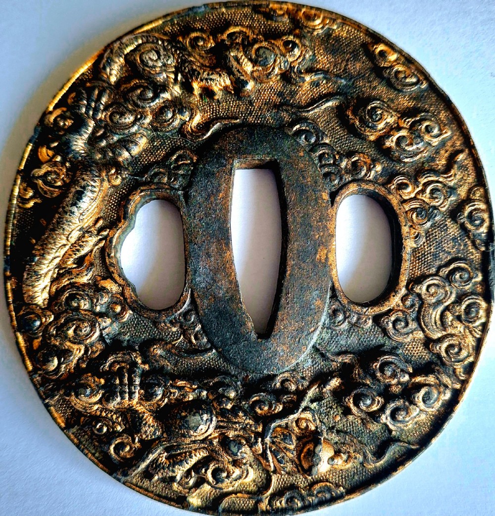 A circular metallic Japanese sword guard featuring a high-relief dragon amongst swirling clouds with central cutouts.