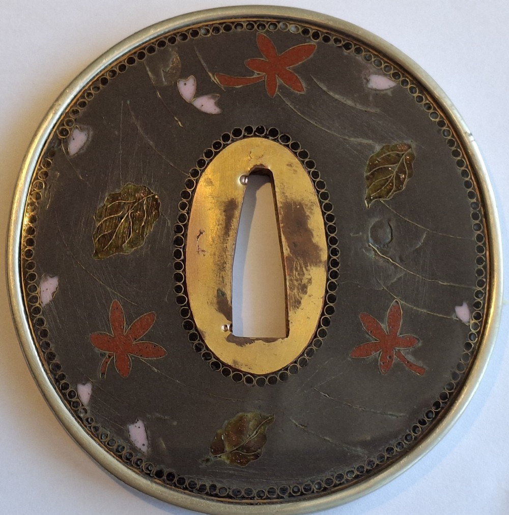 A circular Japanese cloisonne enamel tsuba featuring an intricate figure from folklore set against a dark ground with a central gilt opening. View II