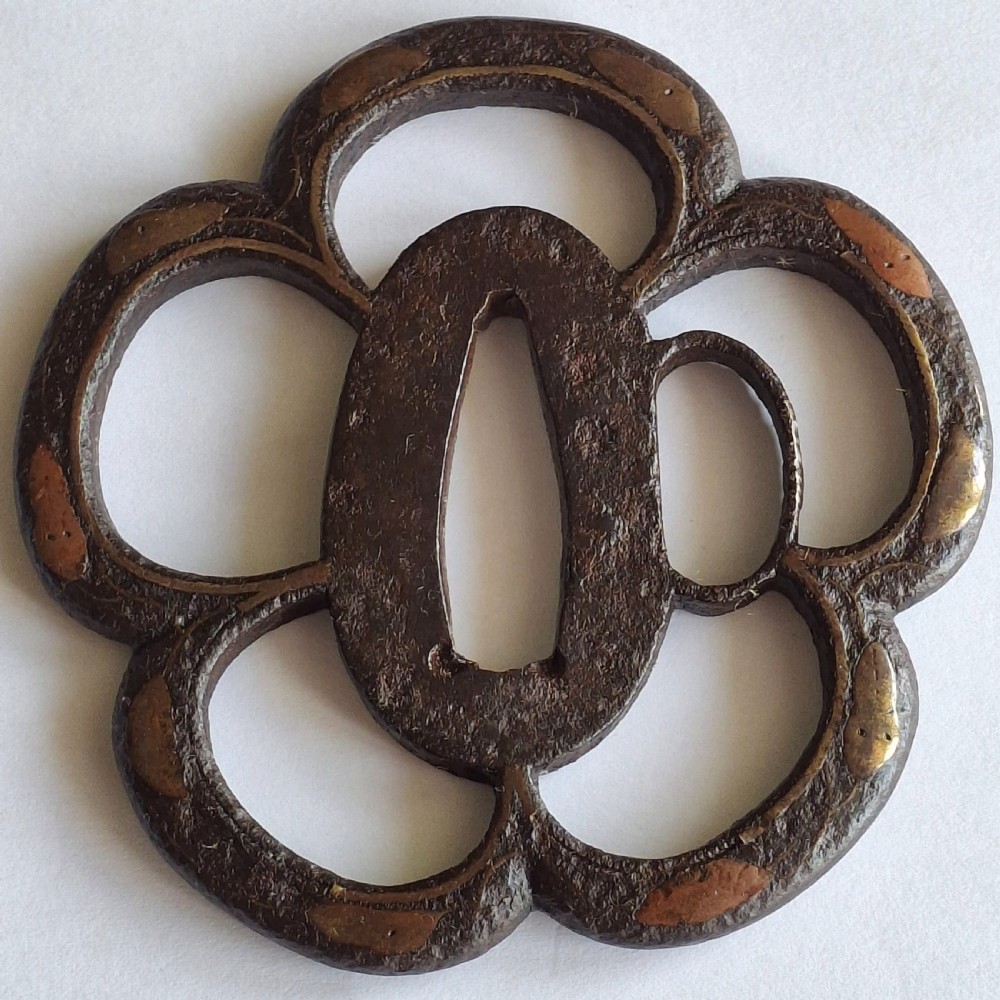 An antique lobed dark iron Japanese tsuba sword guard featuring soft copper inlay detailing around the outer rim and openwork apertures.