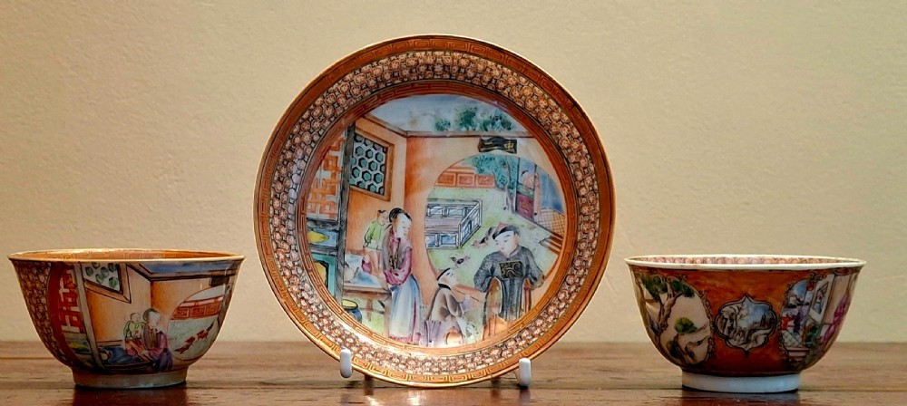 A set of two hand-painted Chinese export porcelain tea bowls and a central matching saucer decorated with figural courtyard scenes and iron-red patterned borders.