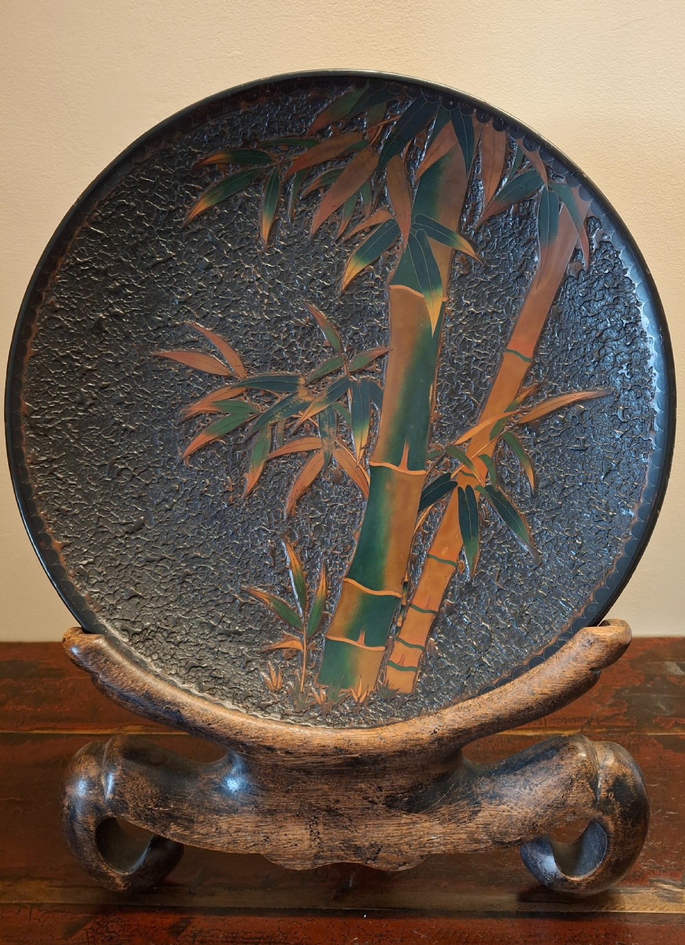 A circular Japanese Totai Shippo charger displaying a textured dark tree-bark surface enamelled with green and terracotta bamboo stalks.