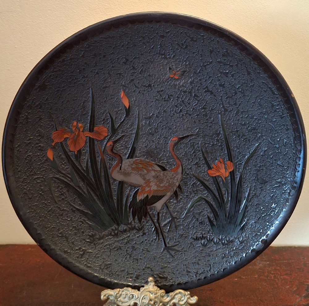 A circular Japanese Totai Shippo ceramic charger plate decorated with a dark textured tree bark ground featuring red-crowned cranes, orange irises, and a butterfly.