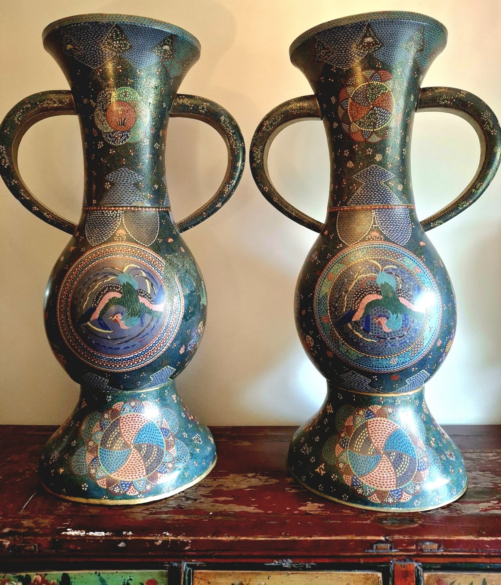 A pair of large Japanese cloisonne enamel vases featuring curved loop handles and intricate blue and green geometric patterns surrounding Ho-o phoenix medallions.