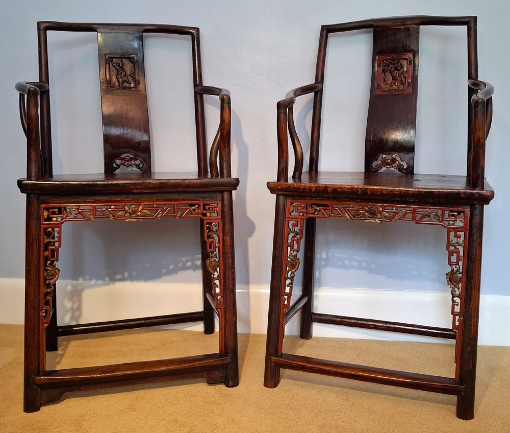 A pair of Chinese dark elm armchairs featuring carved back splat panels and red lacquered decorative aprons.