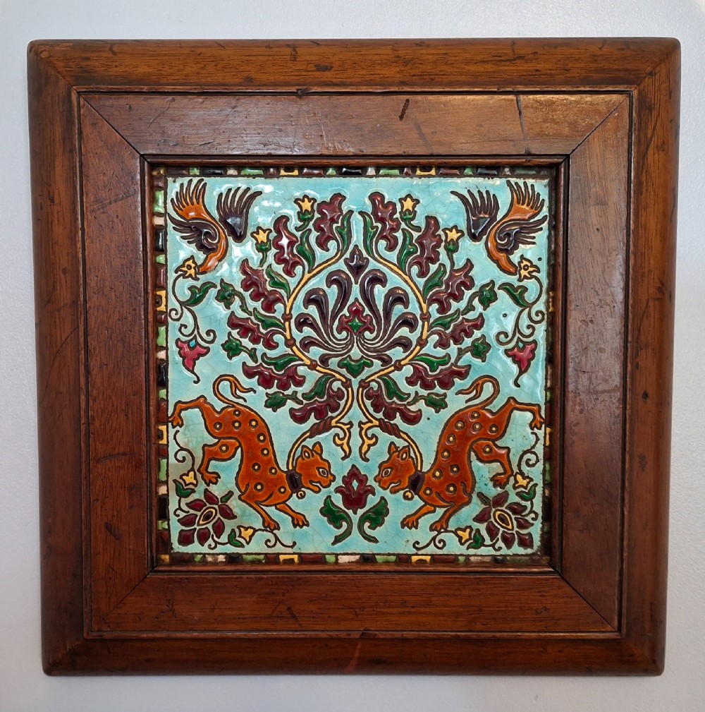 A square French Longwy glazed ceramic tile depicting cheetahs and birds amid foliage, mounted in a dark wooden frame.