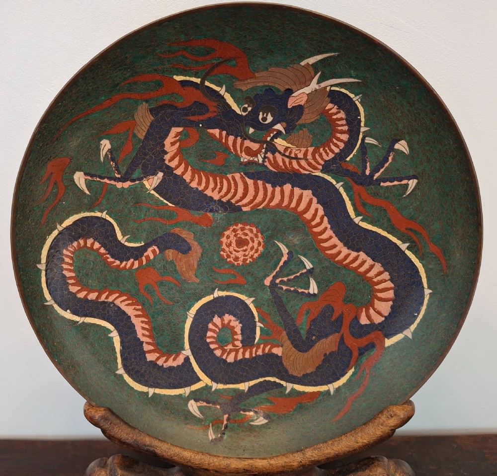 A circular Japanese cloisonne enamel charger featuring a coiling blue and terracotta dragon against a dark green ground with wirework detail.