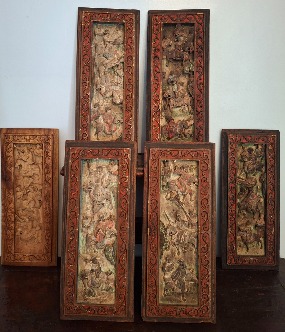 A set of six vertical Chinese carved wooden panels featuring high-relief figures on horseback and ornate decorative borders with traces of red lacquer and gilding.