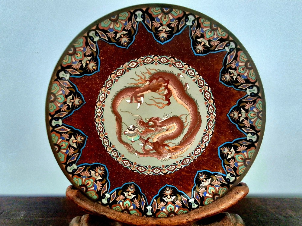 A circular Japanese cloisonne enamel charger depicting a central coiled dragon framed by multi-coloured geometric borders.