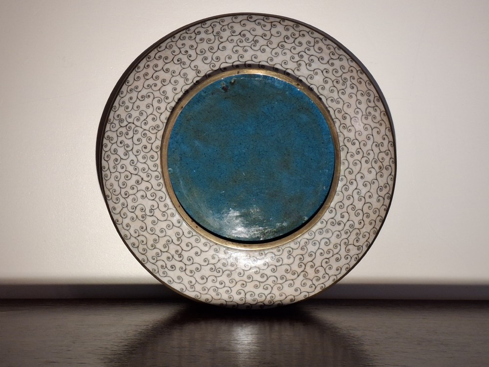 A circular Japanese cloisonne enamel plate featuring a central rectangular panel depicting a samurai warrior in full armour alongside a fan-shaped panel with bamboo foliage, set against a turquoise geometric pattern background. View XII