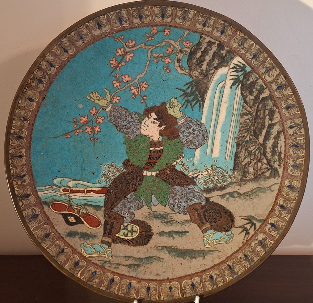 A circular Japanese cloisonne enamel plate depicting a warrior figure beneath a cherry blossom branch and waterfall against a turquoise blue background.
