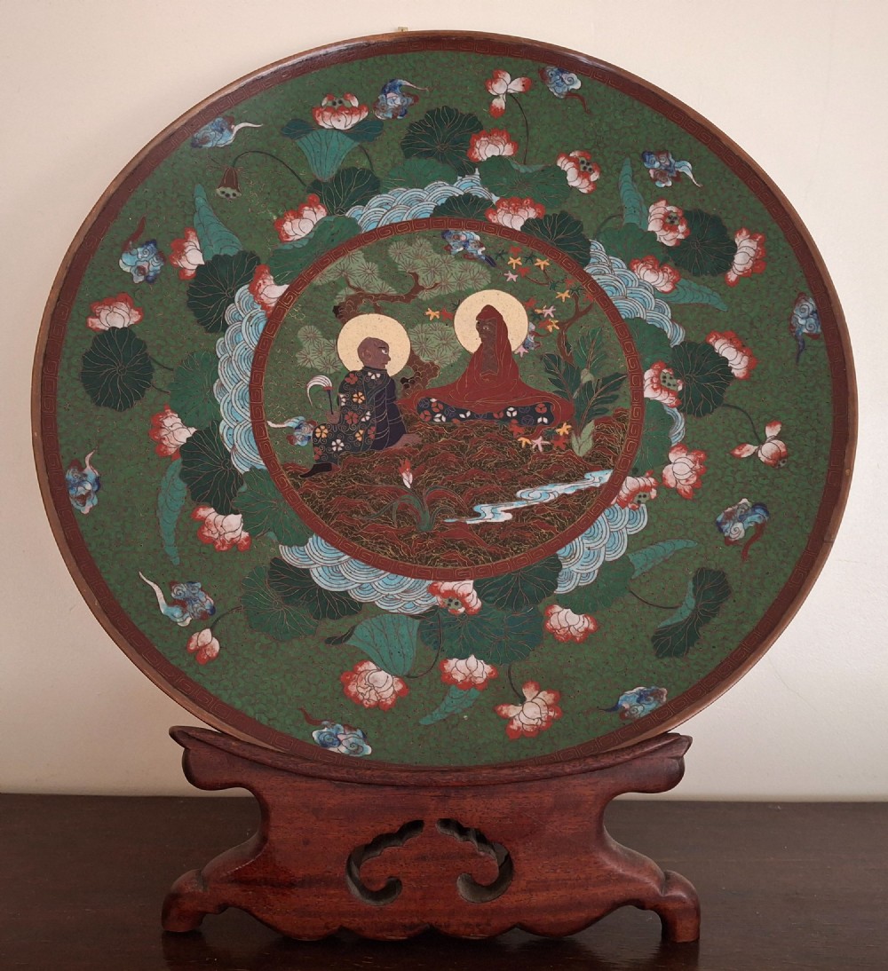 A circular Meiji period Japanese cloisonne enamel charger featuring central haloed figures surrounded by a lotus pattern on a green background.