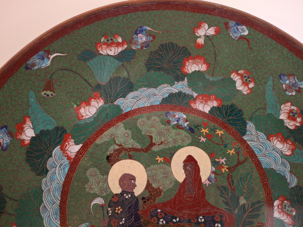 A circular Meiji period Japanese cloisonne enamel charger featuring central haloed figures surrounded by a lotus pattern on a green background. View V