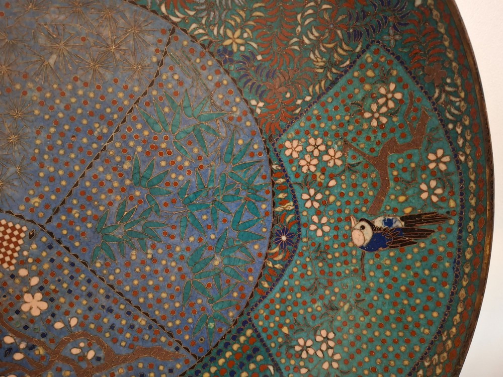 A circular Japanese cloisonne enamel charger decorated with geometric reserves, floral patterns, foliage, and bird motifs in blue, green, and terracotta tones. View V