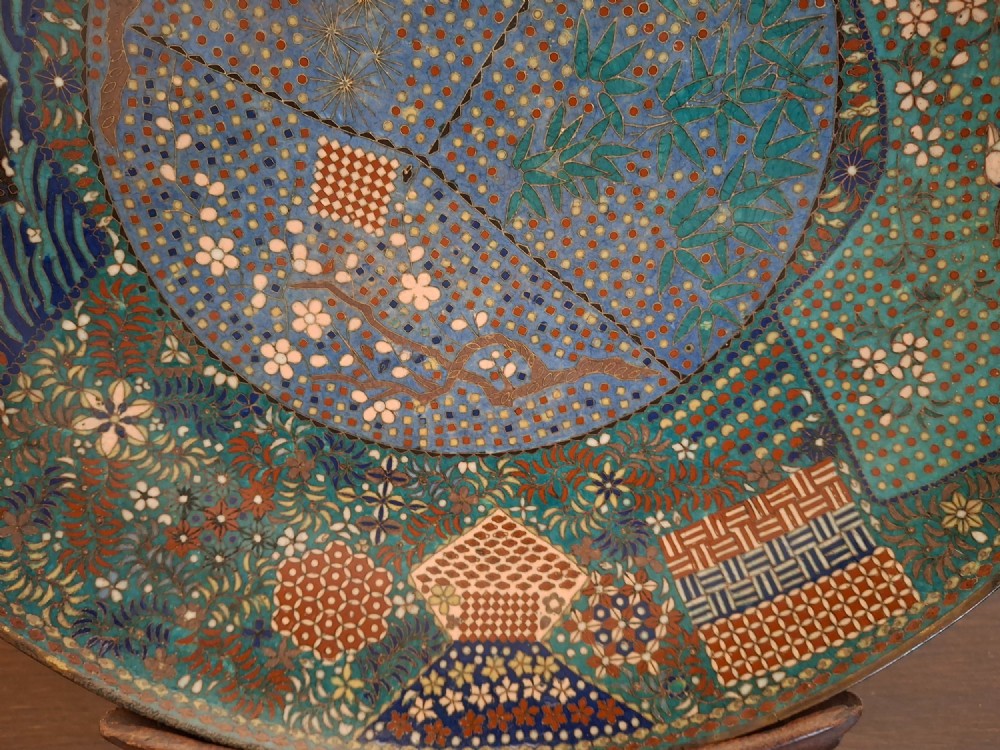 A circular Japanese cloisonne enamel charger decorated with geometric reserves, floral patterns, foliage, and bird motifs in blue, green, and terracotta tones. View VI