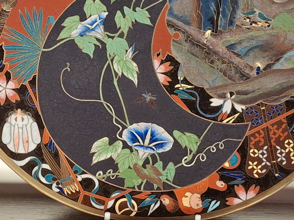 A circular Japanese cloisonne enamel plate featuring intricate floral, landscape, and geometric designs in blue, green, and red against a dark ground. View II